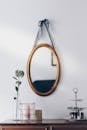 A stylish interior setup featuring a hanging oval mirror with decorative elements on a wooden table.